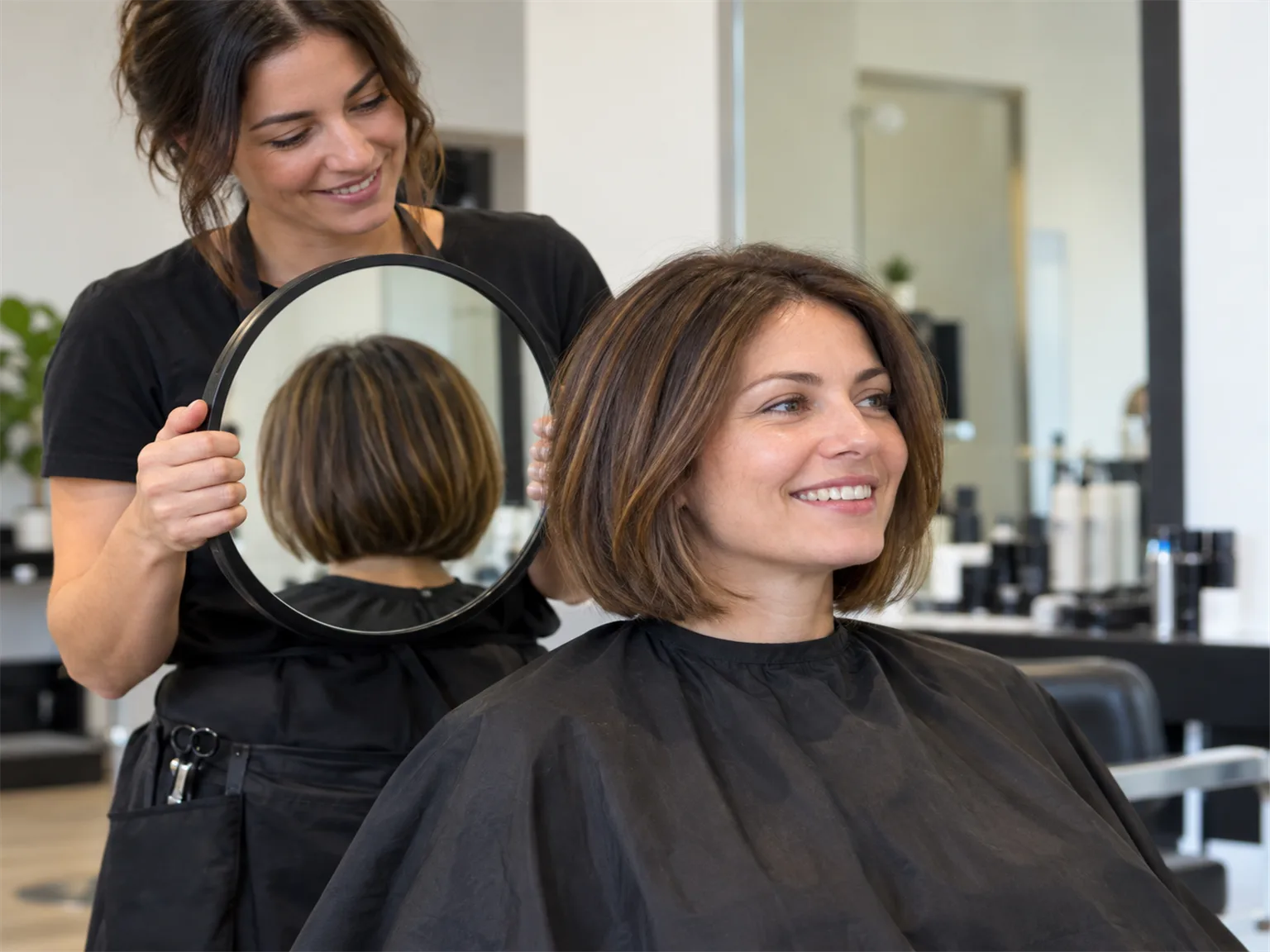 Option I: a hairdresser holding a round mirror behind a client to show the finished haircut